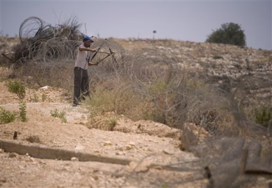 A Palestinian worker cuts barbed wire as he removes an old part of a section of Israel's separation barrier between the outskirts of the West Bank village of Bilin, near Ramallah, and the Jewish settlement of Modiin Illit, on Sunday.
